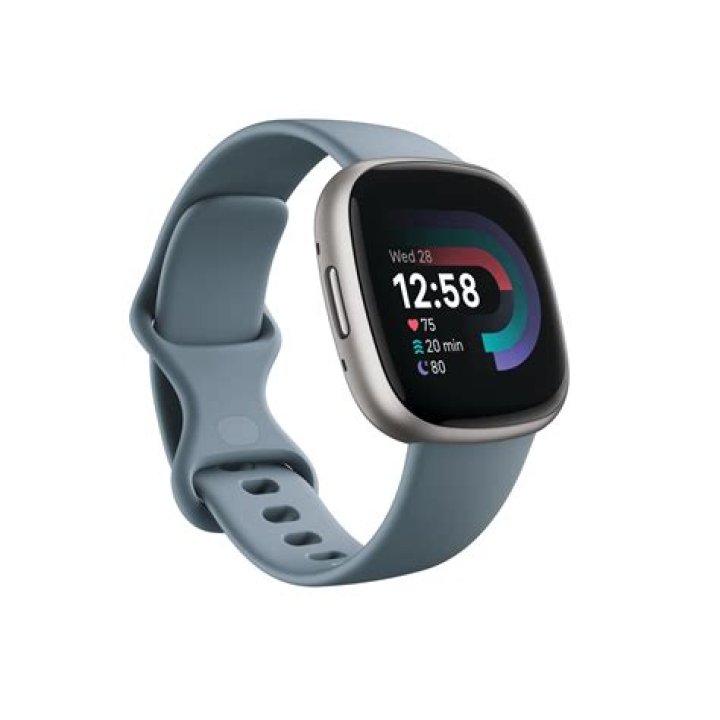 A user holds a Fitbit Charge 5 in hand in front of a green concrete wall.