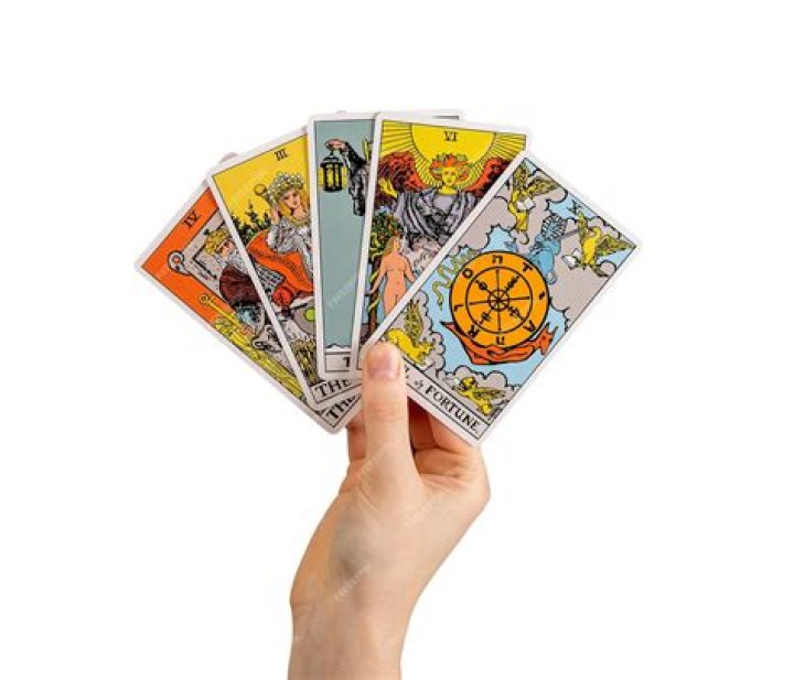 Roya holding tarot cards, surrounded by lit candles, small mirrors, and framed photos